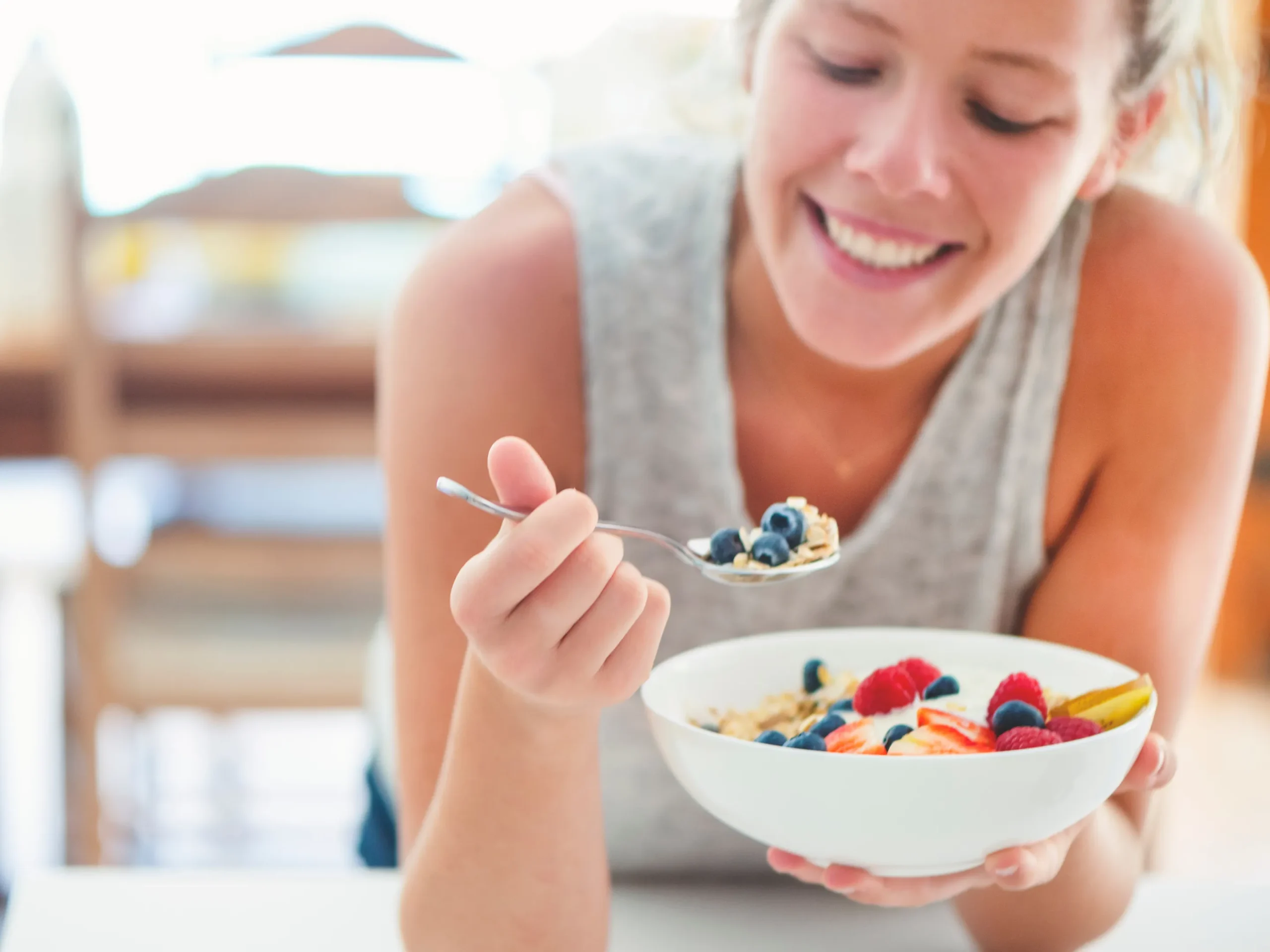woman eating bowl of fruit and yogurt while smiling