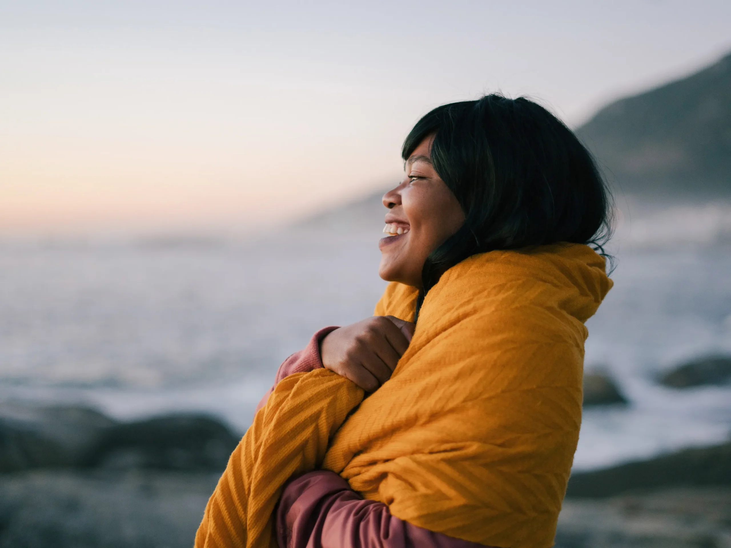 woman smiling wrapped in a blanket looking at the sea
