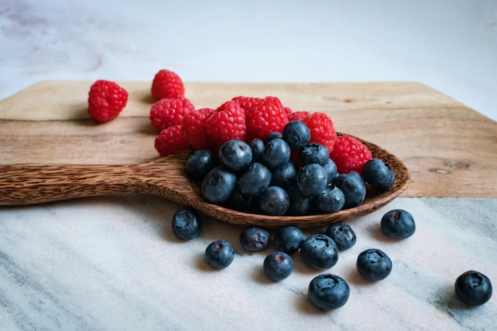 Foods to include in your diet to help PCOS - raspberries and blueberries in a wooden spoon