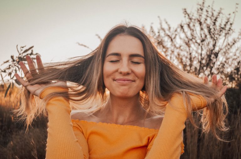 woman standing outside smiling and playing with her hair