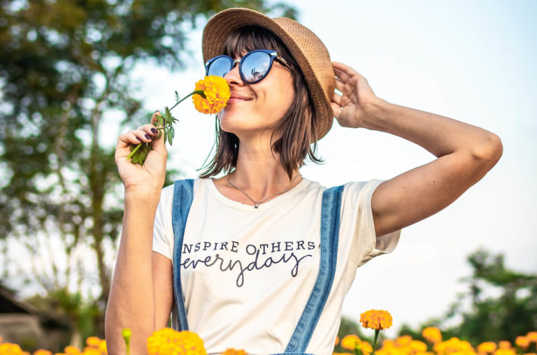 Woman standing in a field of yellow flowers smelling a flower in her hand