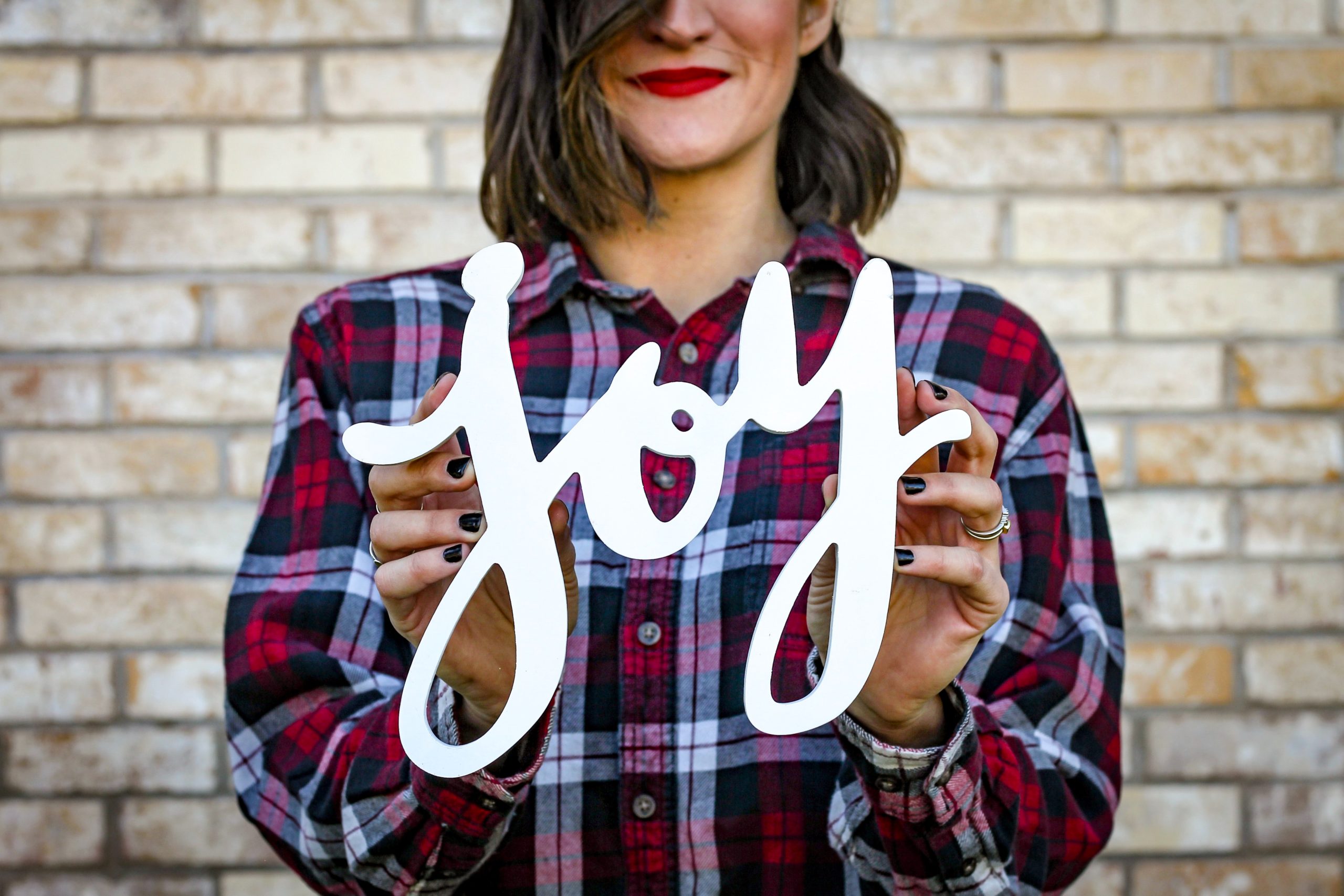 Woman in a flannel shirt holding up a cut out of the word "joy"