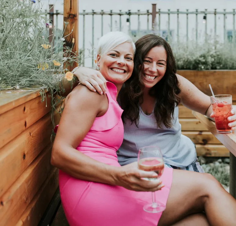 Two woman sitting on a bench with healthy smoothie drinks smiling