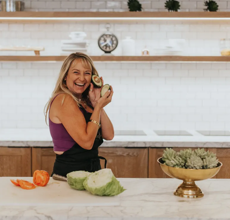 Happy, smiling woman holding an avocado in her kitchen