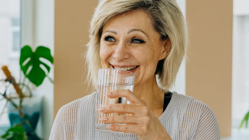 middle-aged woman smiling and staying hydrated by drinking water
