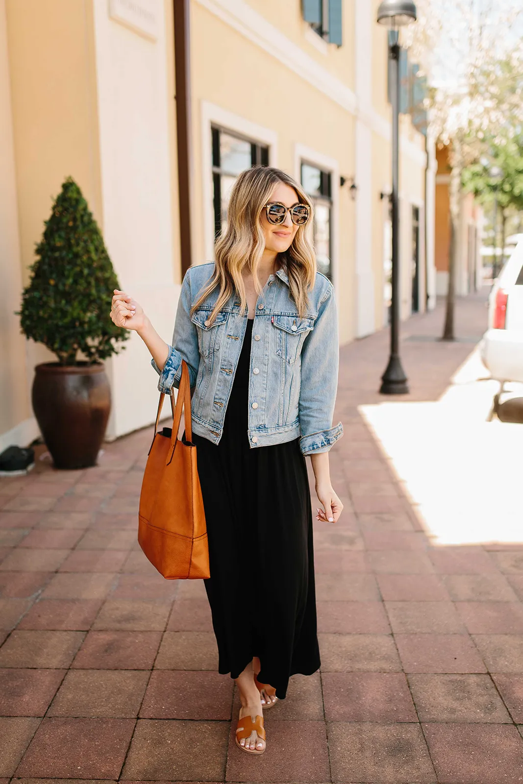 Weekend relaxation outfit - woman wearing black maxi dress with a light blue jean jacket, sunglasses, and a purse
