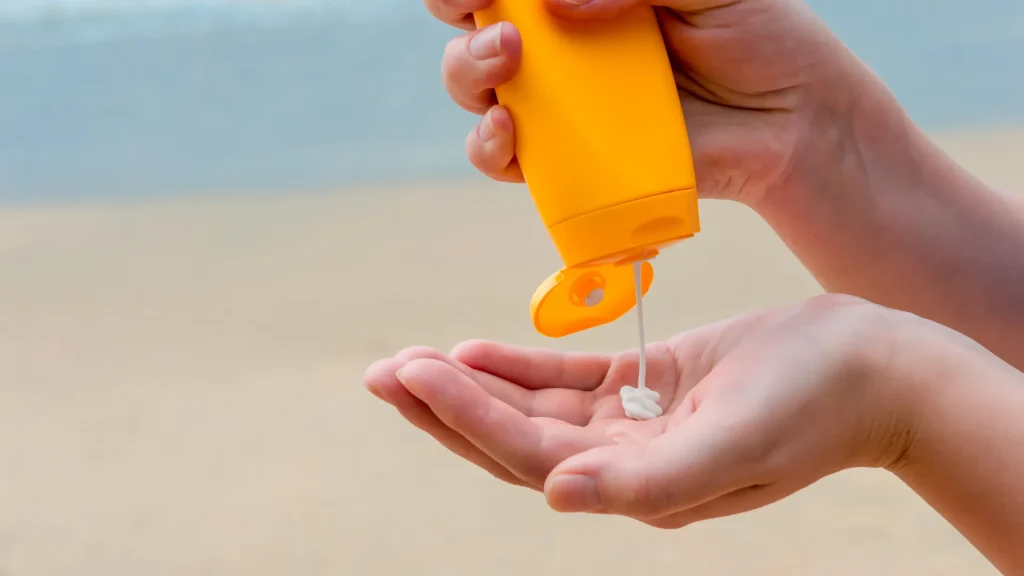 Person squeezing sunblock from orange tube into palm of hand